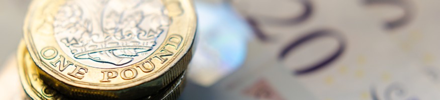 A stack of one pound coins sitting on five and twenty pound notes.